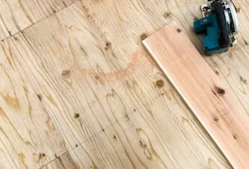 A single board and a saw on a bare subfloor